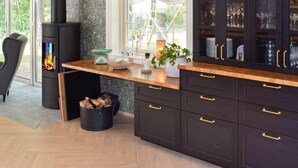 Una cocina moderna con armarios oscuros, encimera de madera y estufa de leña integrada.