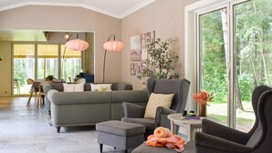 Un salón amplio con un sofá y un sillón grises, y una pequeña mesa con un jarrón de flores. Amplias ventanas ofrecen vistas al exterior.