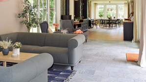 Un salón espacioso con un sofá gris, una mesa de comedor y sillas. Incluye una chimenea, un ventanal grande y una planta.
