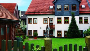 Une rangée de maisons aux toits rouges et aux murs blancs, avec une maison centrale dotée d’un toit bleu et d’un escalier apparent menant à un balcon.