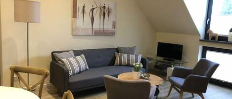 Ein modernes Wohnzimmer mit einem grauen Sofa, zwei Sesseln, einem Couchtisch und einem Fernseher.