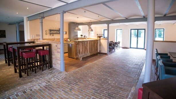 A spacious interior with a kitchen area, dining space, and a large open area with a brick floor. - Holiday Apartment III Bjork (Münchehofe)
