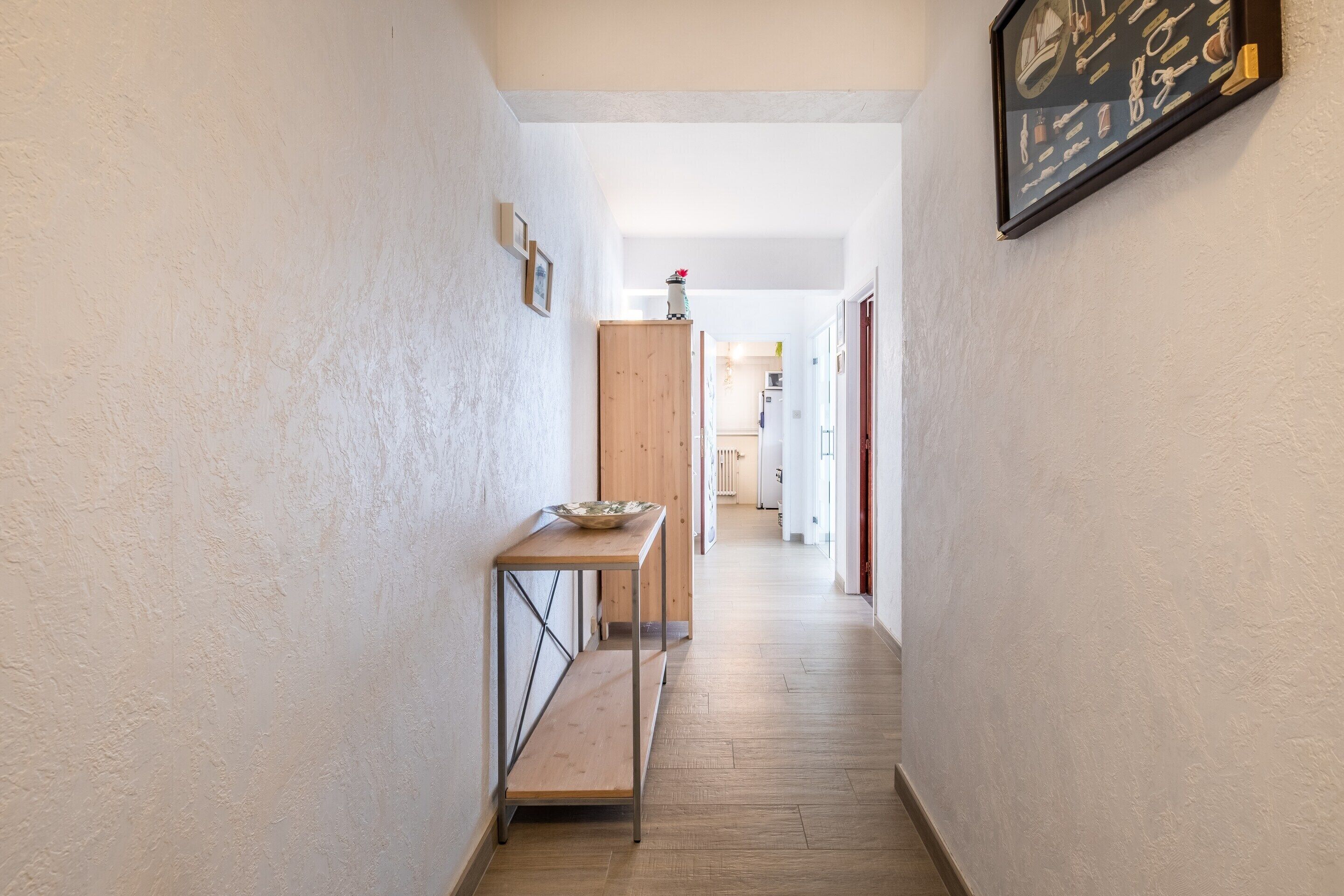Un couloir étroit avec un banc en bois, une petite table et un tableau encadré accroché au mur.