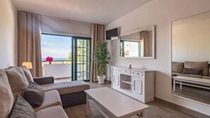 A modern living room with a sofa, a coffee table, a TV, and a balcony with a view.