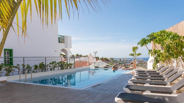 A rooftop pool with lounge chairs, a clear sky, and a view of the cityscape.