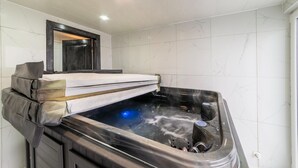 A modern bathroom with a built-in hot tub, a wooden bench, and a mirror above the tub. - Holiday Home in Verviers With Sauna (Verviers)