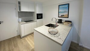 A modern kitchen with white cabinetry, a built-in oven, a stainless steel sink, and a granite countertop. - Apartment in Nieuwpoort With sea Beach (Nieuwpoort)