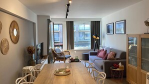 A modern living room with a wooden dining table, white chairs, a sofa, and a cabinet. - Apartment in Nieuwpoort With sea Beach (Nieuwpoort)