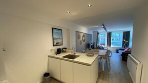 A modern kitchen with a central island, a dining area with a table and chairs, and a living room with a sofa and a lamp. - Apartment in Nieuwpoort With sea Beach (Nieuwpoort)