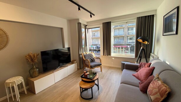 A modern living room with a flat-screen TV, a sofa, a coffee table, and a chair. - Apartment in Nieuwpoort With sea Beach (Nieuwpoort)