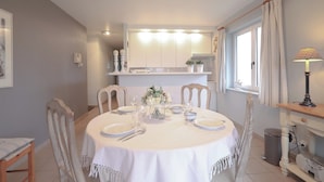 A dining area with a round table set for four, chairs, a vase of flowers, and a lamp on a side table. - Apartment in Belgium Near Coastal Charm (Koksijde)