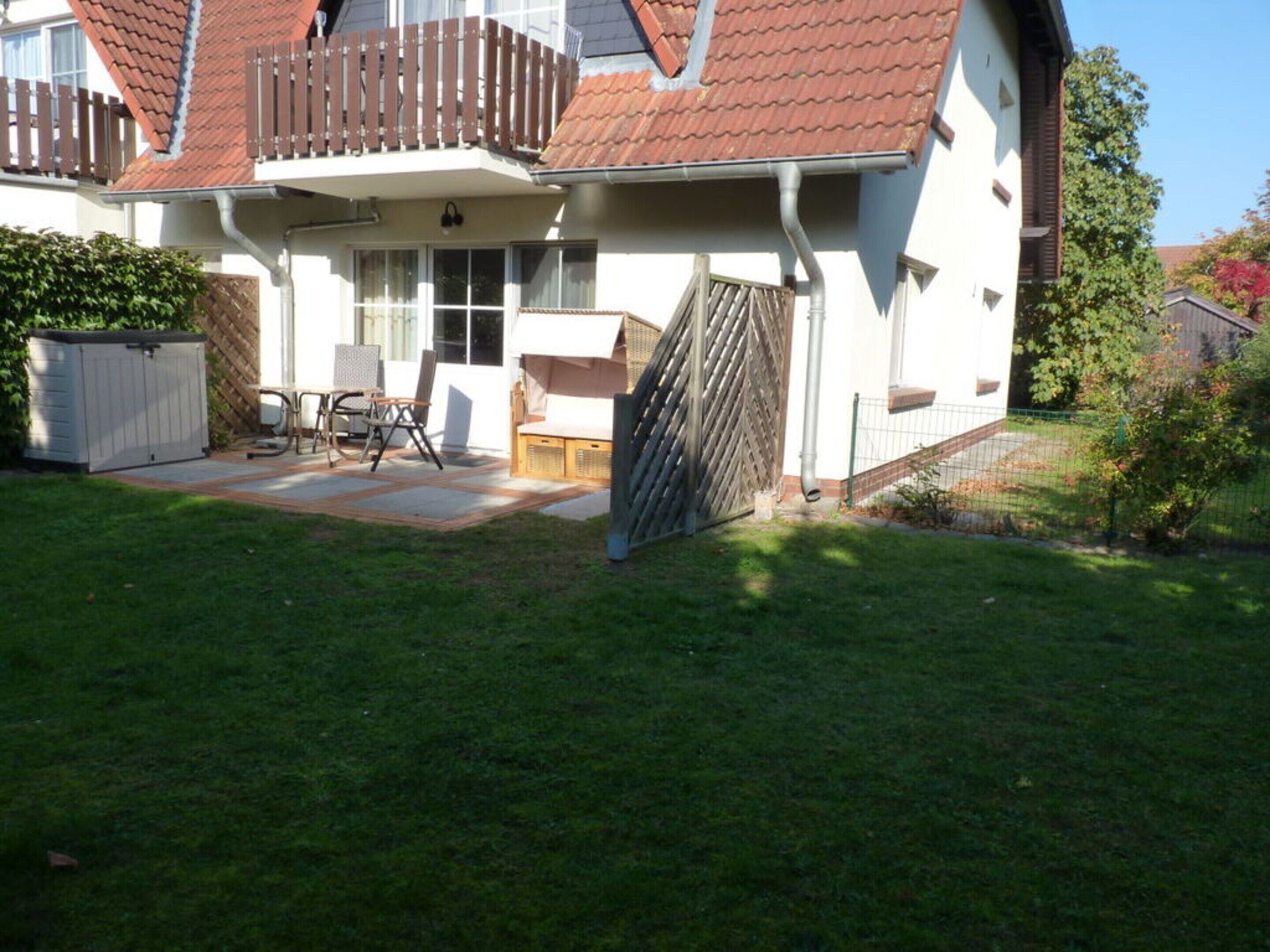 Ein zweistöckiges Haus mit rotem Ziegeldach, einem Balkon und einem umzäunten Garten.
