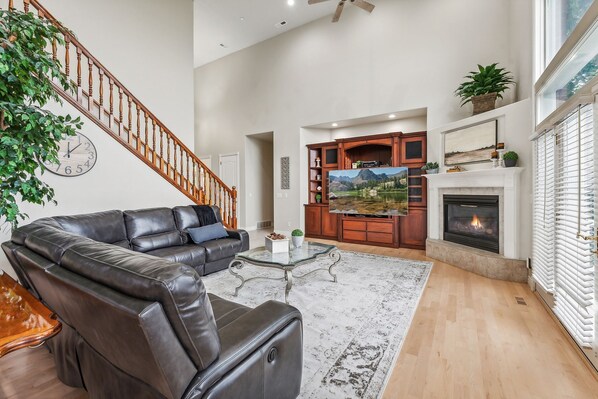 A spacious living room with a leather sofa, a glass coffee table, a fireplace, and a staircase.