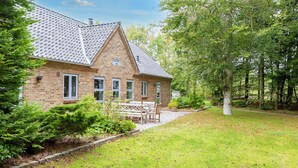 A brick house with a tiled roof, surrounded by a well-maintained lawn and trees.