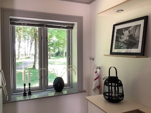 Een kamer met een raam, een vaas, een kandelaar, een handdoek en een ingelijst schilderij aan de muur.