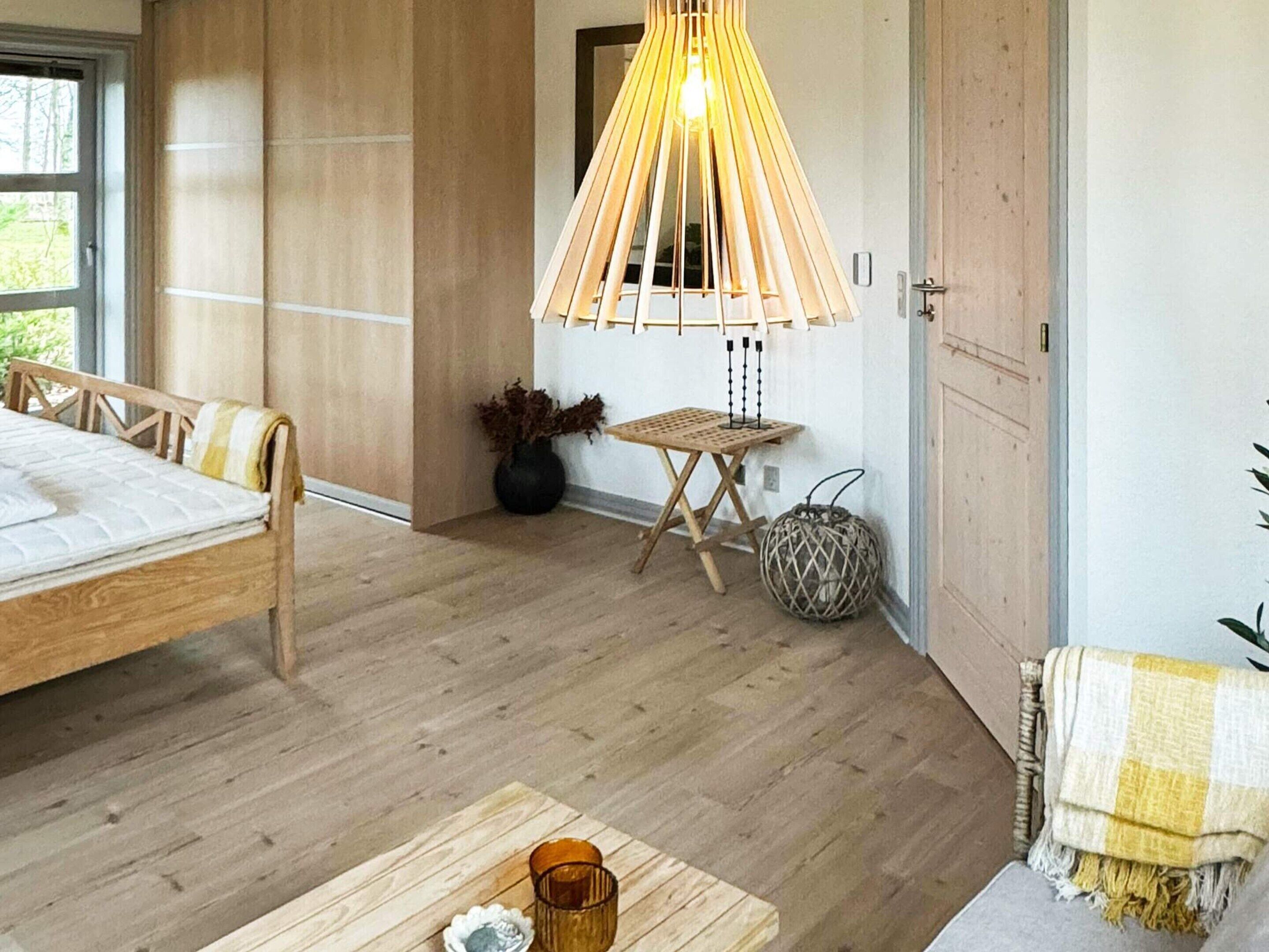 Un dormitorio moderno con una cama de madera, una mesita con un florero y una lámpara colgante.