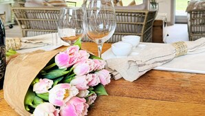 Una mesa de comedor con dos copas de vino, un ramo de flores rosas y una botella de vino.