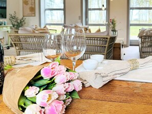 Ein Esstisch mit zwei Weingläsern, einem Strauß pinkfarbener Blumen und einer Weinflasche.