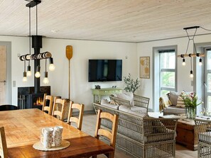 A cozy living room with a wooden dining table, wicker chairs, a fireplace, a television, and a large window. - 8 Person Holiday Home in Thyholm (Thyholm)