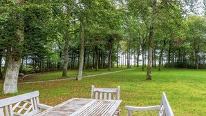 A wooden picnic table and benches in a park with a path and trees.