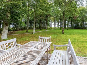 A wooden picnic table and benches in a park with a path and trees.