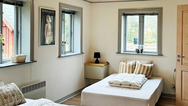 Un dormitorio con dos camas, un radiador, una ventana con cortina y una mesita con lámpara.