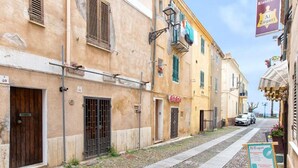 A narrow street lined with buildings, some with shutters and balconies, and a sign for 'Al Tagiuri' restaurant. - Pleasant Apartment in Alghero (Alghero)