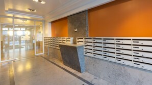 Un área de recepción con mostrador de mármol, puerta de cristal de entrada y pared con buzones.