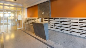 Zona de recepción con mostrador de mármol, buzón empotrado en la pared y puerta de cristal que da a un área de espera.