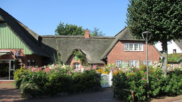 A traditional building with a thatched roof and brick walls, surrounded by lush gardens and a paved pathway. - Holiday Apartment Moby Dick (St. Peter-Ording)