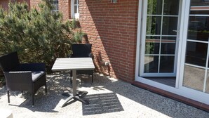 A patio area with a table and chairs, a brick wall, and a sliding glass door. - Holiday Apartment Moby Dick (St. Peter-Ording)