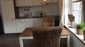 A modern kitchen with white cabinets, a wooden dining table, and a wicker chair. - Holiday Apartment Moby Dick (St. Peter-Ording)