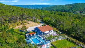 Ein Haus mit Schwimmbecken, umgeben von bewaldeten Hügeln und einem klaren Himmel.