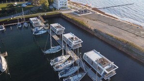 Een jachthaven met diverse boten aangemeerd, een wit gebouw met balkons, en een steiger die in het water uitsteekt.