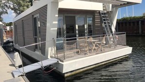 Een modern drijvend huis met een overdekt terras, een trap en een klein zwembad.