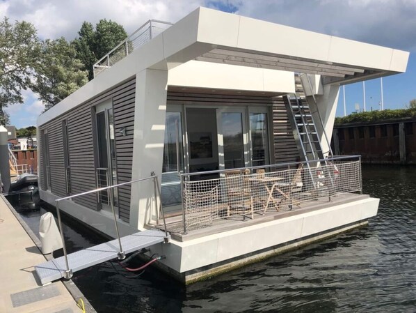 Une maison flottante moderne dotée d’une terrasse couverte, d’un escalier et d’une petite piscine.