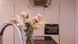 Eine Küche mit einer dunklen Arbeitsplatte, einem Edelstahl-Wasserhahn und einer Vase mit Blumen auf dem Tisch.