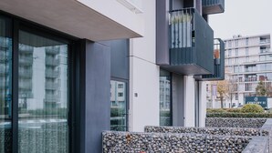 Ein modernes Gebäude mit großen Fenstern, einer Steinwand und einem Balkon mit Pflanzen.
