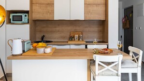 A modern kitchen with wooden cabinets, a central island with a sink, and a dining area with a white chair. - Apartment Good Vibes (Konavle)