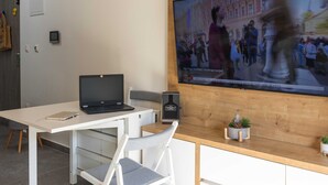 A modern office space with a wooden desk, a laptop, a clock, and a TV displaying a news broadcast. - Apartment Good Vibes (Konavle)