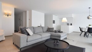 Una sala de estar moderna con un sofá seccional gris, una mesa de centro redonda negra y un comedor con una mesa blanca y sillas negras.