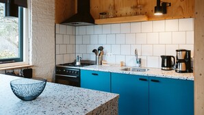 A kitchen with white tiles, blue cabinets, a black range hood, and a window with a view. - Holiday Home Near the sea and Dunes (Ouddorp)