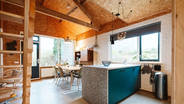 A modern kitchen with a central island, wooden beams on the ceiling, and large windows providing natural light. - Holiday Home Near the sea and Dunes (Ouddorp)