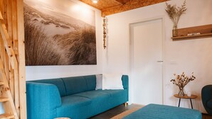 A modern living room with a blue sofa, a small round table with a vase, and a wooden ladder. - Holiday Home Near the sea and Dunes (Ouddorp)