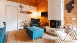 A cozy living room with a fireplace, a television mounted on the wall, and a comfortable seating area with a sofa and ottoman. - Holiday Home Near the sea and Dunes (Ouddorp)