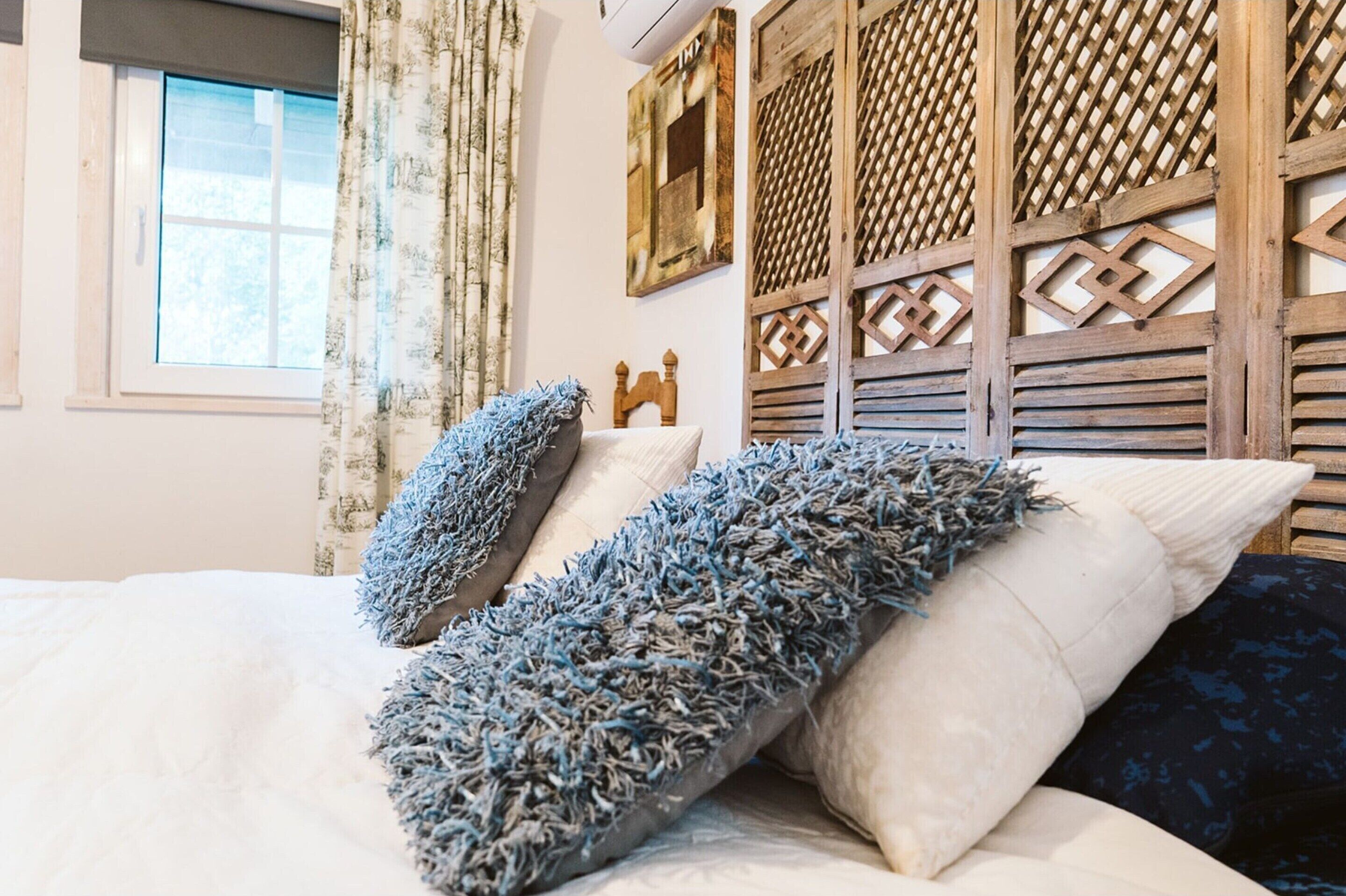 Une chambre à coucher avec un lit, des oreillers, une fenêtre avec des rideaux et un panneau décoratif au mur.