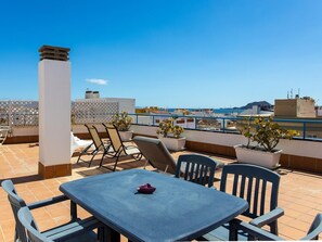 A rooftop terrace with a table and chairs, potted plants, and a view of the cityscape. - Belvilla by OYO Uptown III (La Oliva)