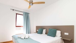 A bedroom with a bed, a ceiling fan, a window with curtains, and a wall-mounted shelf.