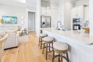A modern kitchen with white cabinetry, a stainless steel refrigerator, a microwave, and a large island with stools.