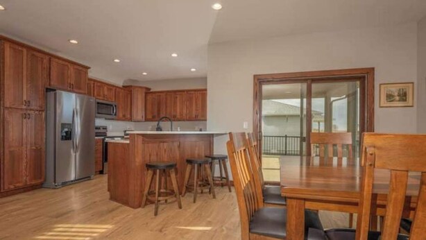 Una cocina moderna con armarios de madera, un refrigerador de acero inoxidable y una barra con taburetes.